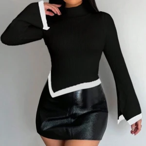 Ny. Svart stickad tröja med vit kant - Snygg svart stickad tröja med vit kant längs ärmslut och nederkant. Tröjan har lång ärm, hög hals och asymmetrisk nederdel som ger en cool och modern look. Perfekt för dig som gillar stilrena detaljer och vill sticka ut lite extra. Aldrig använd.