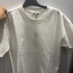 Vit Set från Stone Island - Vit Set från Stone Island med klassisk rund hals och korta ärmar. Ikonisk svart och gul Stone Island patch sitter fast på ena ärmen. T-shirten& Shorts  är i mjuk bomull och har en clean, stilren look som passar perfekt till streetwear. Först till kvarn🫡🙌🏼