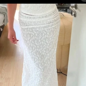 Vit lång spetskjol med broderi - Superfin lång kjol i vit spets med broderade detaljer och lätt transparent känsla. Kjolen har en feminin och romantisk look med vackert mönster och sitter snyggt i midjan. Perfekt för sommarens alla tillfällen!