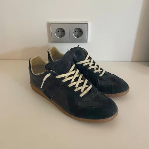 Maison Margiela mörkblå sneakers - Säljer ett par Maison Margiela skor i storlek 43.  Skorna är i bra skick men ändå tecken på användning. Både box och dustbad finns! Nypris på dessa skor ligger på lite under 9k men säljer för endast 3499, kvitto finns även vid befrågan. Obs tar emot bud!