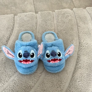 Blå Stitch tofflor med 3D-öron - Supermjuka och fluffiga tofflor i blått med Stitch-ansikte och stora 3D-öron. Perfekta för dig som älskar Disney och vill ha något gulligt och bekvämt på fötterna hemma. Insidan är också mjuk och värmande.