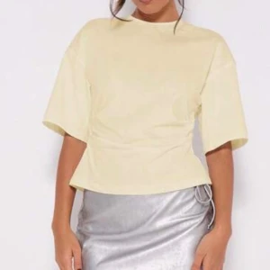 Ljusgul topp med omlottdetalj - Snygg ljusgul topp med korta ärmar och rund hals. Toppen har en unik omlottdetalj baktill och lätt markerad midja som ger en cool siluett. Perfekt att styla med kjol eller jeans för en trendig look. Nu med prislapp