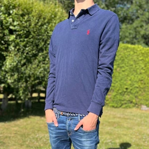 👕 Marinblå Ralph Lauren Pikétröja - Slim Fit 🧵 -  👕 Marinblå Ralph Lauren Pikétröja - Slim Fit 🧵  *   Storlek: M (men sitter som en S!) *   Passform: Slim fit *   Detaljer:     *   Klassisk krage med knappar vid halsen     *   Röd broderad Ralph Lauren-logga på bröstet ❤️ *   Material: 100% bomull - mjuk och skön! ☁️ *   Modell: 176 cm, ca 63 kg 🏋️‍♂️ *   Skick: Perfekt för en stilren look! ✨ HÖR AV DIG VID MINSTA FUNDERING😁 
