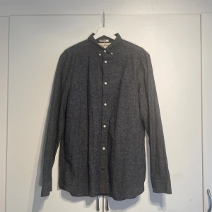 Mörkgrå skjorta från H&M L.O.G.G. - Snygg mörkgrå skjorta från H&M L.O.G.G. i regular fit. Skjortan har klassisk krage med knappar, vita knappar framtill och en bröstficka. Tillverkad i bomull och passar perfekt till jeans eller chinos. storlek M och true to size. Sparsamt använd och är i fint skick. Hör av dig för fler bilder. 