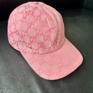 Rosa Gucci keps med GG-mönster - Snygg rosa keps från Gucci med ikoniskt GG-monogram över hela kepsen. Kepsen har böjd skärm, justerbart band bak och en liten guldfärgad GG-detalj framtill. Tillverkad i bomullstyg med exklusiv känsla och perfekt för dig som vill sticka ut.