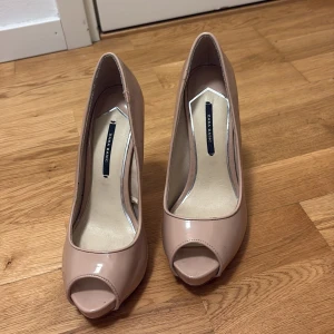 Beige peep-toe pumps från Zara Basic - Snygga beige pumps från Zara Basic med hög klack och öppen tå. Skorna har en stilren design med lackad finish och plattform framtill. Perfekta för dig som vill ha en klassisk men trendig look.