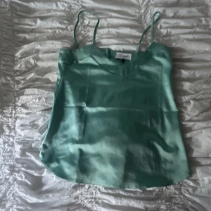 Turkos linnetopp från Closet London - Snygg turkos linnetopp från Closet London i glansigt satinliknande material. Tunn och luftig med smala axelband och v-ringning. Perfekt för varma dagar eller när du vill ha en stilren look med lite extra shine.