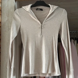 Ribbad beige långärmad tröja Bik Bok - Superskön ribbad tröja från Bik Bok i beige med lång ärm och halv dragkedja framtill. Tröjan har en snygg krage och är figurnära i modellen, perfekt att styla med jeans eller kjol.