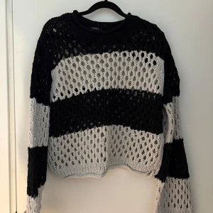 Randig stickad tröja från Lindex - Säljer en stickad tröja från Lindex i storlek S. Tröjan har breda svarta och, är grovstickad med hålmönster och har lång ärm. Perfekt för lager-på-lager och ger en cool, avslappnad vibe.