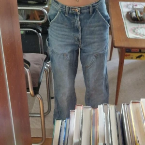 BDG High-Rise Carpenter Jeans, stl 28 - Säljer ett par ljusblå high-rise carpenter jeans från BDG Urban Outfitters. Byxorna har breda ben, flera praktiska fickor på sidorna och klassisk jeanslook. Perfekt för dig som gillar en loose och avslappnad stil. Lite slitage nere på ena benet (se bild 5). 