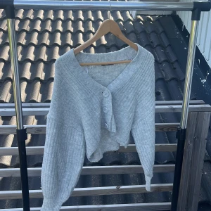 Ljusgrå kofta från Gina Tricot - Supermjuk ljusgrå kofta från Gina Tricot i ribbstickad design. Koftan har v-ringning, stora knappar framtill och en croppad, loose passform med långa ärmar. Perfekt att slänga över en topp för en chill look.