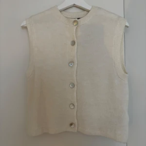 Beige stickad väst från Gina Tricot - Supermjuk beige stickad väst från Gina Tricot med rund hals och snygga pärlemorknappar framtill. Västen är ärmlös och har en rak, lite loose passform som är enkel att styla över en skjorta eller t-shirt. Aldrig använd!