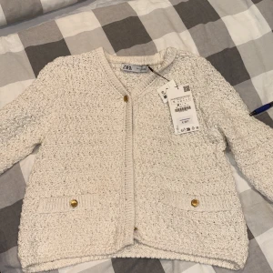 Beige stickad kofta från Zara - Superfin beige stickad kofta från Zara med snygg struktur, guldknappar framtill och på fickorna. Koftan har långärmad passform och är perfekt för lager-på-lager. Enkel att matcha med både jeans och kjol.