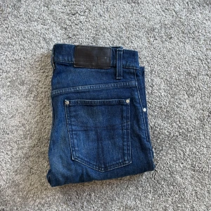 Blå jeans från Tiger of Sweden - Snygga blå jeans från Tiger of Sweden med klassisk femficksdesign och diskreta slitningar. Jeansen har slim passform och är tillverkade i denim av bomull. Perfekta för dig som gillar stilrena och tidlösa jeans.