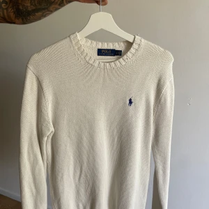 Vit stickad tröja från Polo Ralph Lauren - Vit stickad tröja från Polo Ralph Lauren med klassisk rund halsringning och blå broderad logga på bröstet. Skick 9/10 väldigt snygg tröja 