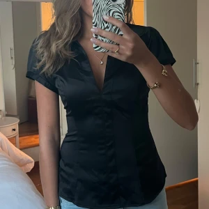 Svart figursydd kortärmad sidenskjorta - Säljer en svart, figursydd sidenskjorta med korta ärmar och djup v-ringning. Säljer denna då den inte passade mig. (de två första bilderna är original bilderna från hon som jag köpte den av) !köparen står för frakten!