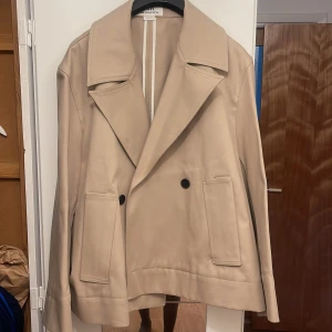 Beige skepparkavaj från Zara Man Edition - Stilren beige skepparkavaj från Zara Man Edition SS'24 med bred krage, dubbla knappar och stora fickor framtill. Jackan har en klassisk rak passform och är tillverkad i ett mjukt material som känns lyxigt. Perfekt för dig som gillar minimalistisk och clean stil.