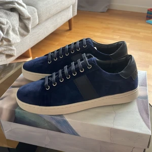 Mörkblå mockasneakers från The Gallerist - Snygga sneakers i mörkblå mocka med svarta skinnpartier och vita sulor. Skorna har klassisk snörning. Insidan har färgglad stänkmönstrad sula. Perfekta för dig som gillar stilrena men unika detaljer. Jag säljer skorna för att de är för små i storleken för mig och skorna är helt nya så de är i sitt bästa skick!!