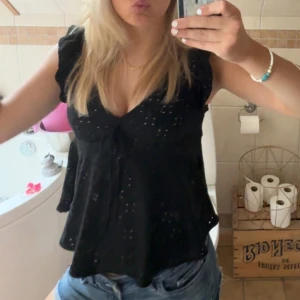 Jättegullig svart blus med knyt och volanger - Supersöt svart blus med v-ringning, volangärmar och knyt framtill. 