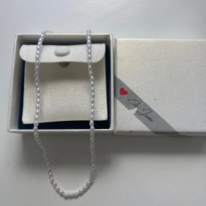 Pärlhalsband från Cilla Jeweler - Ett elegant halsband med vita ovala pärlor från Cilla Jeweler. Halsbandet har en klassisk design med små, glansiga pärlor och ett diskret guldfärgat lås. Perfekt för dig som gillar stilrena smycken med tidlös känsla.