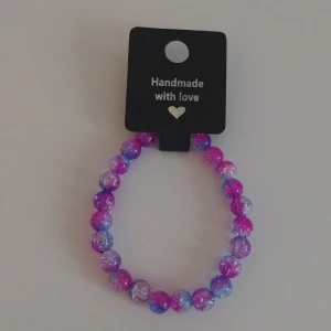 Färgglatt pärlarmband i rosa och lila - Handgjort armband med runda pärlor i rosa, lila och blå toner. Pärlorna har en glittrig och spräcklig effekt som ger ett unikt och lekfullt intryck. Perfekt accessoar för att addera färg till din outfit.