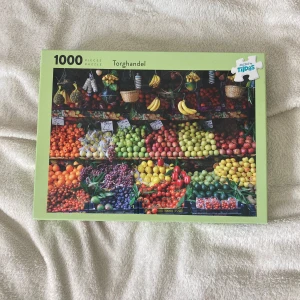 Torghandel - Färgglatt 1000-bitars pussel med motiv av en livlig frukt- och grönsaksmarknad. Perfekt för dig som gillar utmaningar och vill ha en snygg bild att lägga tillsammans med vänner eller familj. Skapa en riktig färgexplosion hemma!