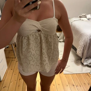 Beige virkad och broderad linnetopp - Supersöt beige linnetopp med virkad överdel och broderade blommor på den luftiga nederdelen. Toppen har smala axelband och twistad detalj framtill. Perfekt för varma dagar och ger en romantisk vibe.