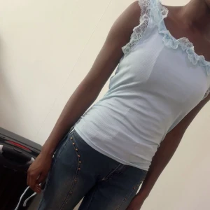 Ljusblå ribbad linnetopp med spets - Supersöt ljusblå linnetopp med ribbad struktur och romantiska spetsdetaljer runt axlar och urringning. Toppen är ärmlös och har en tight passform som framhäver siluetten. Perfekt för dig som gillar en feminin och trendig look.