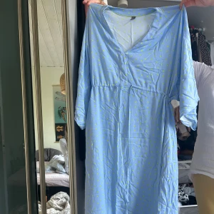 Ljusblå långklänning med prickar - Söt ljusblå långklänning med små gula prickar och trekvartsärm. Klänningen har omlottknytning i midjan och v-ringad hals. Perfekt för dig som gillar en avslappnad och somrig stil.