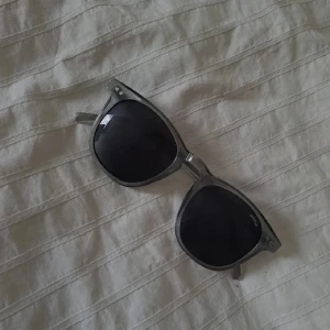 Grå transparenta solglasögon Prestige - Snygga solglasögon från Prestige med transparent grå båge och svarta glas. Klassisk form som passar till många stilar. Perfekta för soliga dagar.