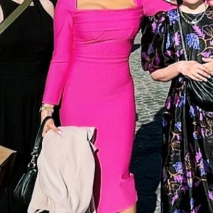 Chockrosa långärmad klänning - Säljer en chockrosa, figurnära klänning med långa ärmar och snygg draperad urringning. Klänningen är knälång och har dragkedja i ryggen. Materialet är stretchigt och känns lyxigt. Perfekt för dig som vill sticka ut med en färgstark look!