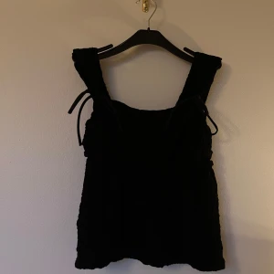 Svart topp med rosetter - Svart topp i storlek S från Ginatricot, med breda axelband och knytband på axlarna (Endast detalj, inte justerbar). Toppen har skrynkligt material. Skriv privat om du vill ha fler bilder🤍Även oanvänd, endast testad!