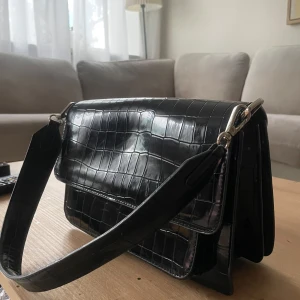 Svart axelväska i lackat crocomönster - Knappt använd mellanstor handväska. Inköpt på Åhléns City för några år sedan men kan inte minnas vilket märke det var. 