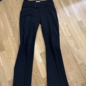 Svarta bootcut kostymbyxor - Snygga svarta kostymbyxor med bootcut passform och pressveck. Byxorna har låg midja, två knappar i midjan och bälteshällor.  Materialet känns mjukt och byxan är stretchig. Strl 164. Gina tricot Young. Använd 1-2 ggr. Köpta för 300kr
