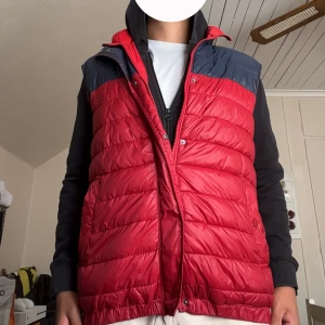 Röd dunväst från Divided by H&M - Snygg röd dunväst från Divided by H&M med mörkblå axelparti. Västen är quiltad och har både dragkedja och tryckknappar framtill. Perfekt för lager-på-lager och funkar till många olika stilar. Två fickor med knappstängning på sidorna. Skick 8/10 Hör av dig om de är något du undrar över☺️ Priset ej hugget i sten🤩