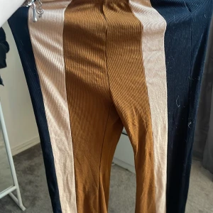 Randiga ribbade byxor i brunt och svart - Unika ribbade byxor med breda vertikala ränder i brunt, beige och svart. Byxorna har elastisk midja och är i stretchigt material som ger en skön passform. Perfekta för dig som vill sticka ut med en cool och färgstark look.