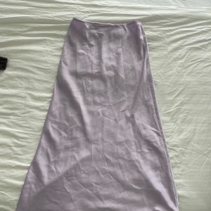 Ljuslila långkjol i satin - Supersnygg ljuslila långkjol i satin med lätt glansig finish. Kjolen har en enkel och stilren design med lätt utsvängd form som ger en flowy känsla. 