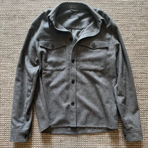 Grå overshirt från J.Lindeberg - Snygg grå overshirt från J.Lindeberg i ullmix.. Perfekt lager-på-lager och är perfekt nu till hösten. Stilren och enkel att matcha till olika outfits. Är i 9/10 skick och i storleken M. Om du har några funderingar är det bara att höra av dig / mvh William! 