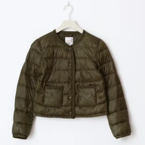Olivgrön quiltad pufferjacka - Snygg olivgrön pufferjacka från Gina med rund halsringning och tryckknappar framtill. Jackan är quiltad, har två stora fickor fram och är croppad i modellen. Perfekt för dig som vill ha en stilren och trendig look. Storleken är 146-152💕💕