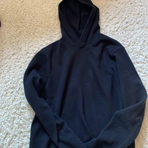 Cashmere Hoodie  - Enkel svart hoodie med huva och långa ärmar. Modellen är klassisk och passar dig som gillar en clean och stilren look. Tröjan är i mjukt material och har ribbade muddar vid ärmslut och nederkant. Perfekt för chill dagar eller när du vill ha något bekvämt.