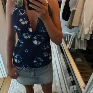 Blå batik halterneck linne - Supersnygg blå halterneck linne med batikmönster i vitt. v-ringning framtill och öppen rygg med knyt i nacken. Perfekt för varma dagar och ger en riktigt somrig vibe. Sitter tajt över bysten och har en figurnära passform. 
