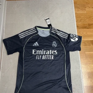 Real Madrid Mbappé fotbollströja Adidas - Snygg marinblå Real Madrid fotbollströja från Adidas med Mbappé och nummer 9 på ryggen. Tröjan har korta ärmar, vita detaljer och klubbmärke på bröstet. Tillverkad i lätt och ventilerande material, perfekt för match eller träning. Priset kan diskuteras