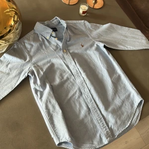 Ljusblå skjorta från Ralph Lauren - (Pris:239kr inklusive frakt)Klassisk ljusblå skjorta från Ralph Lauren med broderad logga på bröstet. Skjortan har lång ärm, knappar framtill och button down-krage. Tillverkad i mjuk bomull och passar perfekt till en clean och stilren look.