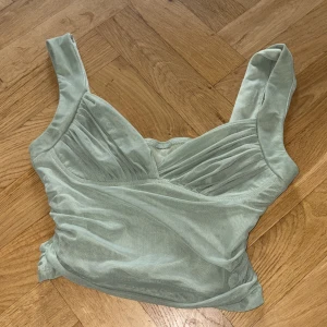 Ljusgrön omlottopp från SHEIN - Supersöt ljusgrön omlottopp från SHEIN med breda axelband och snygga rynkade detaljer över bysten. Toppen är figurnära och har en mjuk, stretchig känsla tack vare materialet i polyester och elastan. Perfekt att styla med jeans eller kjol för en fräsch look.