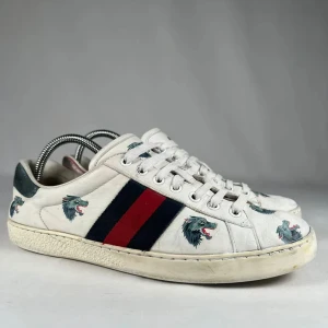 Gucci sneakers med vargmotiv - Snygga vita sneakers från Gucci med klassiska blå och röda ränder på sidan. Skorna har broderade varghuvuden i grönt och blått samt detaljer i mörkgrönt skinn på hälen. Perfekta för dig som vill sticka ut med exklusiv streetstyle.