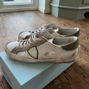 Philippe Model vita sneakers - Snygga vita sneakers från Philippe Model med detaljer i beige mocka och klassisk snörning. Skorna har rund tå, platt sula och diskret logga på sidan. Perfekta för en clean och avslappnad look. Materialmix av skinn och mocka ger en lyxig känsla. Skorna har en liten blå prick som man dock inte ser när man bär dom, de kanske också går att tvätta bort men har aldrig testat😁🙌.