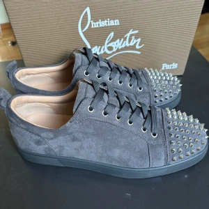 Christian Louboutin - Mörkgråa sneakers i mocka från Christian Louboutin med ikonisk röd sula och silverfärgade nitar på tån. Skorna har snörning och rund tå, samt lyxig läderinsida. Perfekt för dig som vill sticka ut med en edgy och exklusiv look. Skriv om det är något ni undrar. Boxen och påsen till skorna samt og fås med vid köp. Priset går att diskutera under snabb affär.