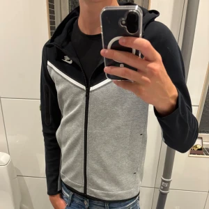 Nike tech fleece - Oanvänd och stilren Nike tech fleece i färgerna grå och svart. Praktisk ficka med dragkedja på ena ärmen och sportig look. Perfekt för dig som gillar streetstyle. Pris kan diskuteras vid snabb affär! Vid frågor eller funderingar så ska du inte tveka på att höra av dig!🙌