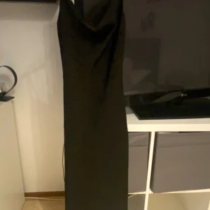 Svart lång satinklänning - Snygg svart långklänning i satin med smala axelband och elegant, enkel design. Klänningen har en lätt glansig yta och rak passform som ger en stilren look. Perfekt för dig som vill ha en klassisk och tidlös stil.