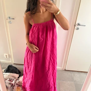 Rosa långklänning med tunna axelband - Säljer en superfin långklänning i stark rosa färg med tunna axelband och avslappnad passform. Klänningen har en enkel och luftig design, perfekt för varma dagar. Materialet känns lätt och svalt mot huden.